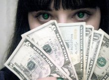 Девушка брюнетка держит перед лицом веер из долларов