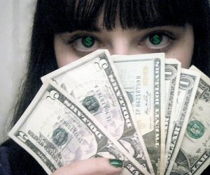 Девушка брюнетка держит перед лицом веер из долларов